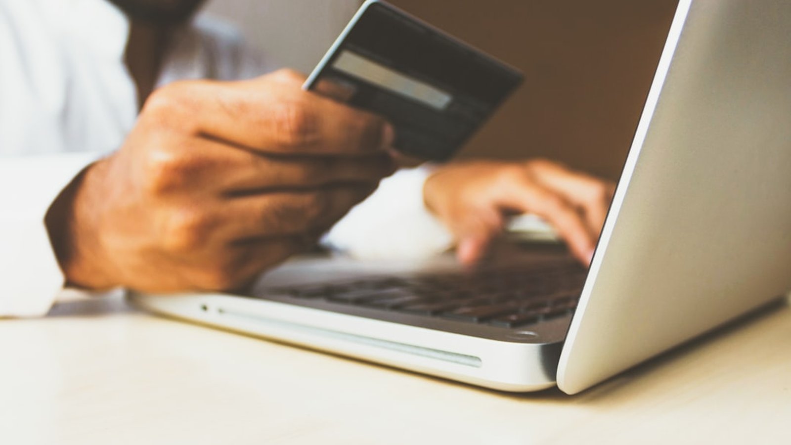 A person using a laptop while holding a payment card