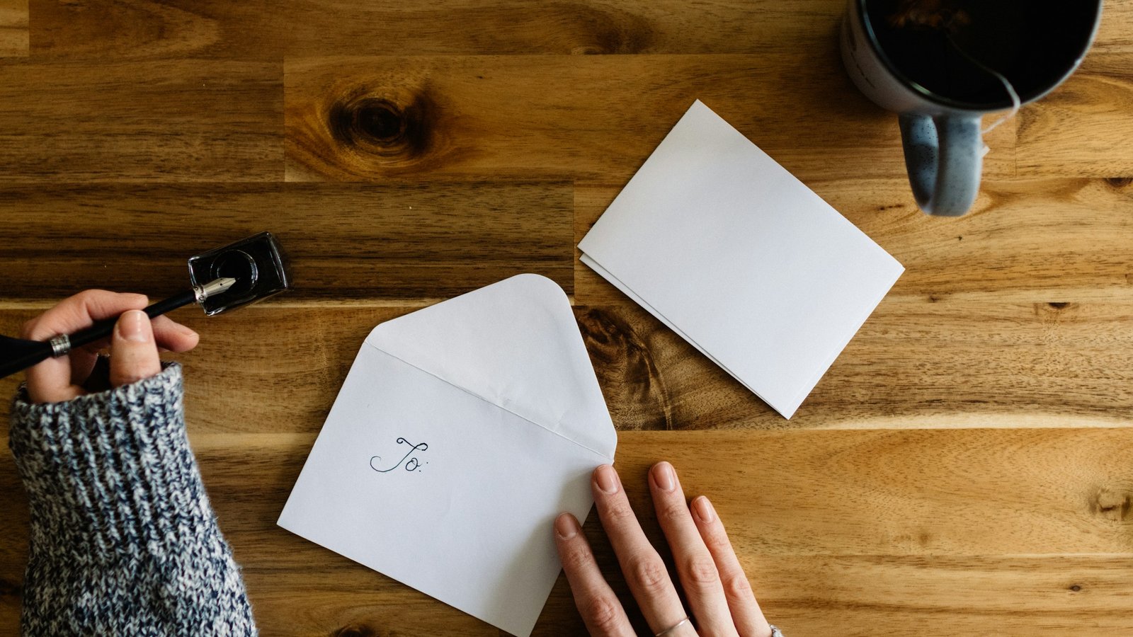 A person writing on a sheet of paper at a table next to a cup of coffee