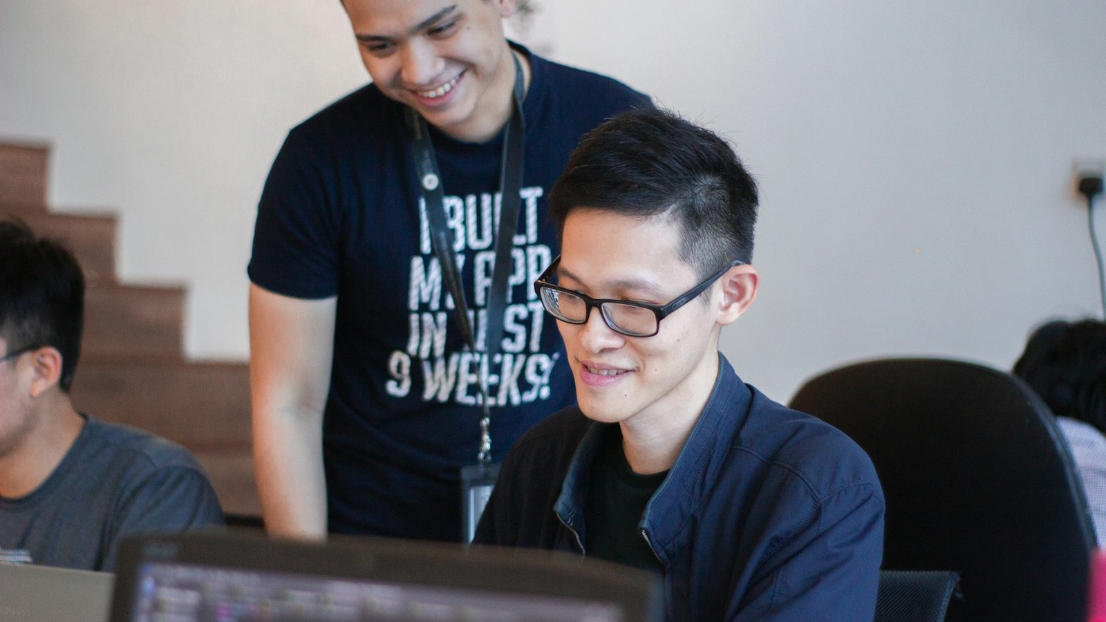 A mentor standing behind a seated developer, looking at code together on a screen