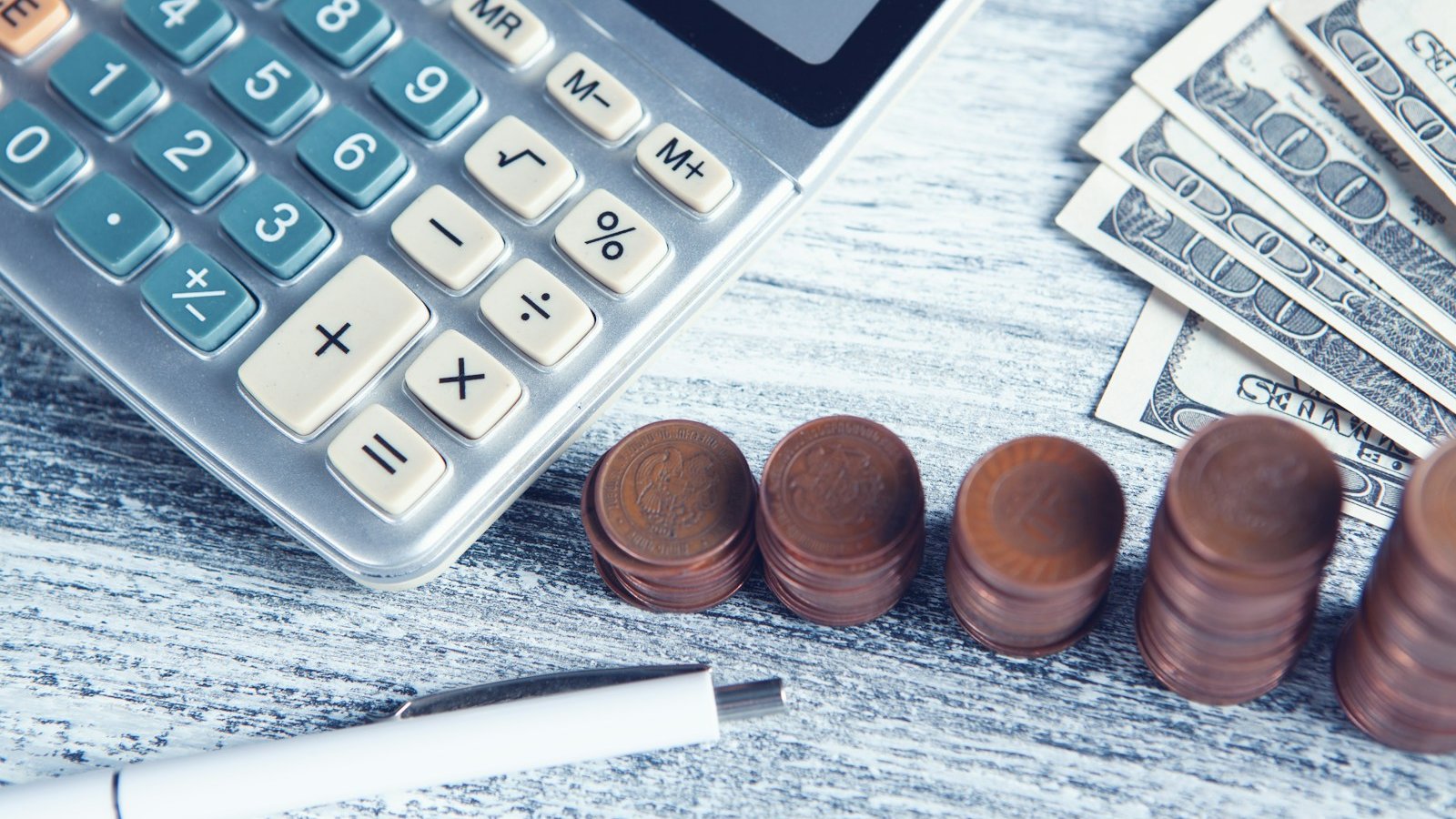 A calculator, a pen, and folded money on a wooden table