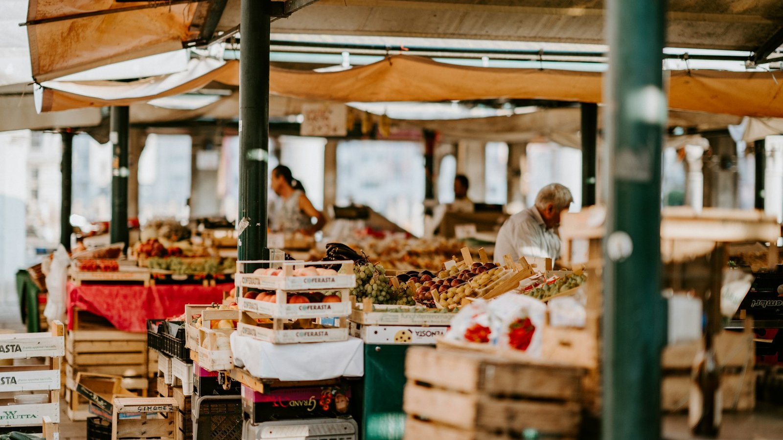A fruit and vegetable market stall with a vendor arranging produce