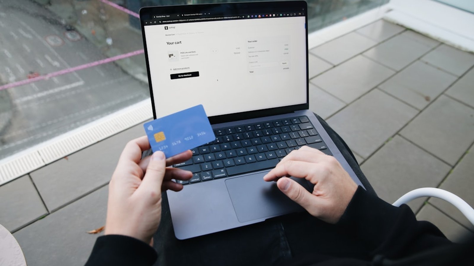 A person sitting with a laptop holding a credit card to make an online payment