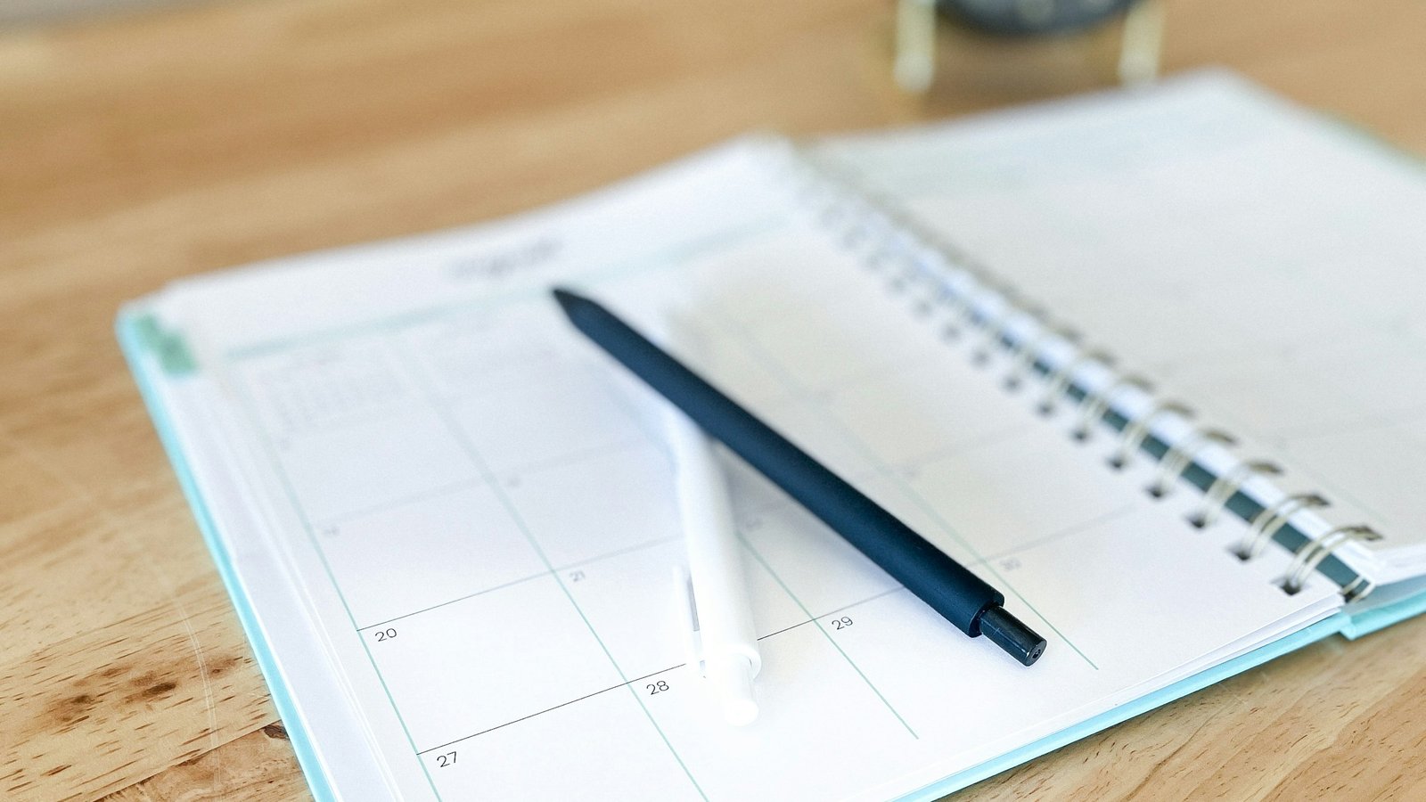 An open paper planner with a pen resting on it, on a wooden desk